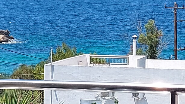 Vista costera con mar azul cristalino, algunos veleros y un edificio con balcón con vistas al océano.