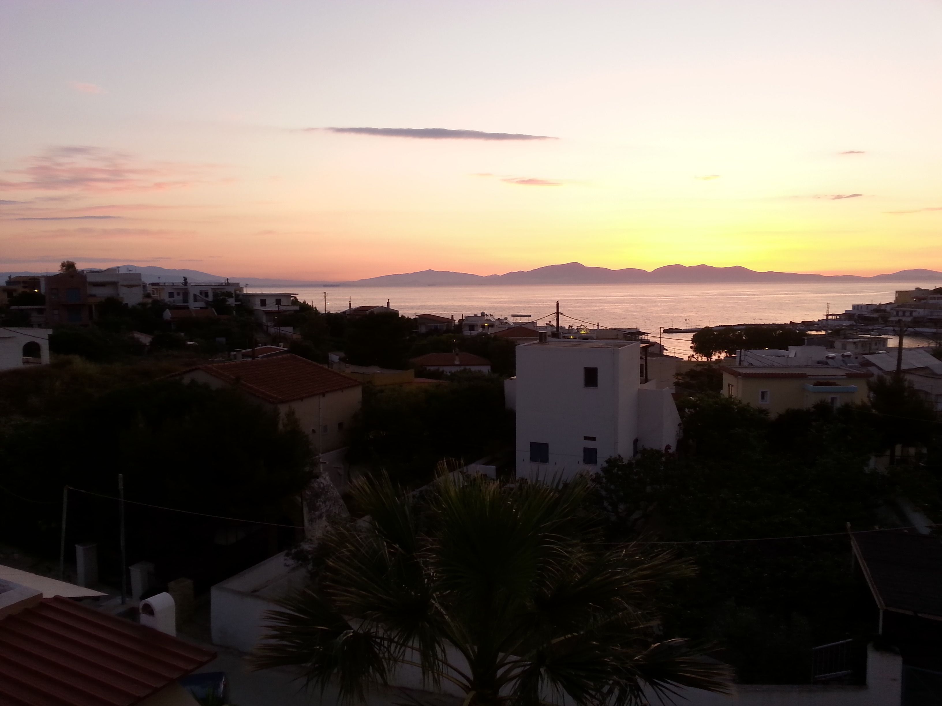 A coastal town at sunset with buildings and a view of the sea.