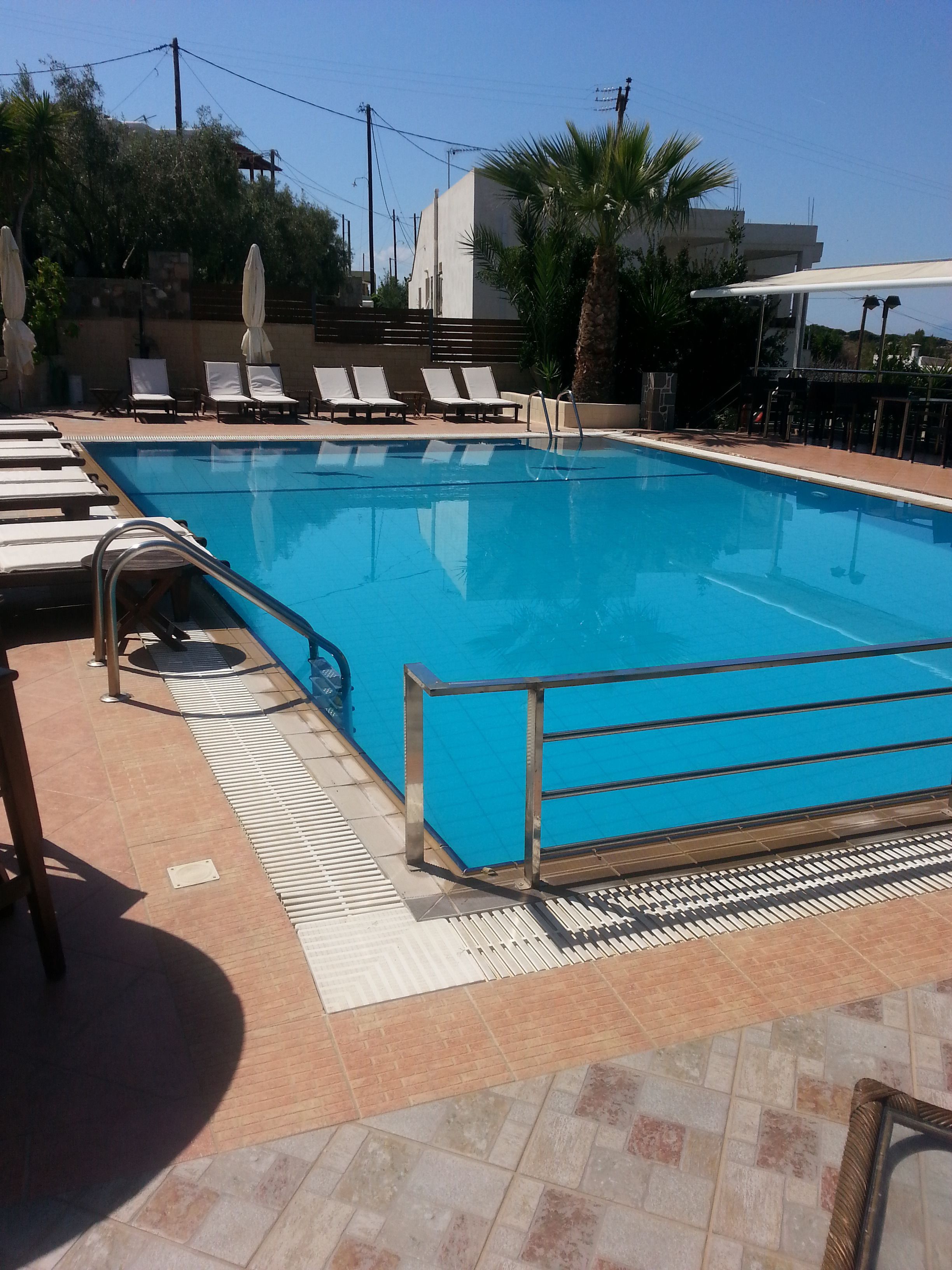 A swimming pool with sun loungers and a tiled deck.
