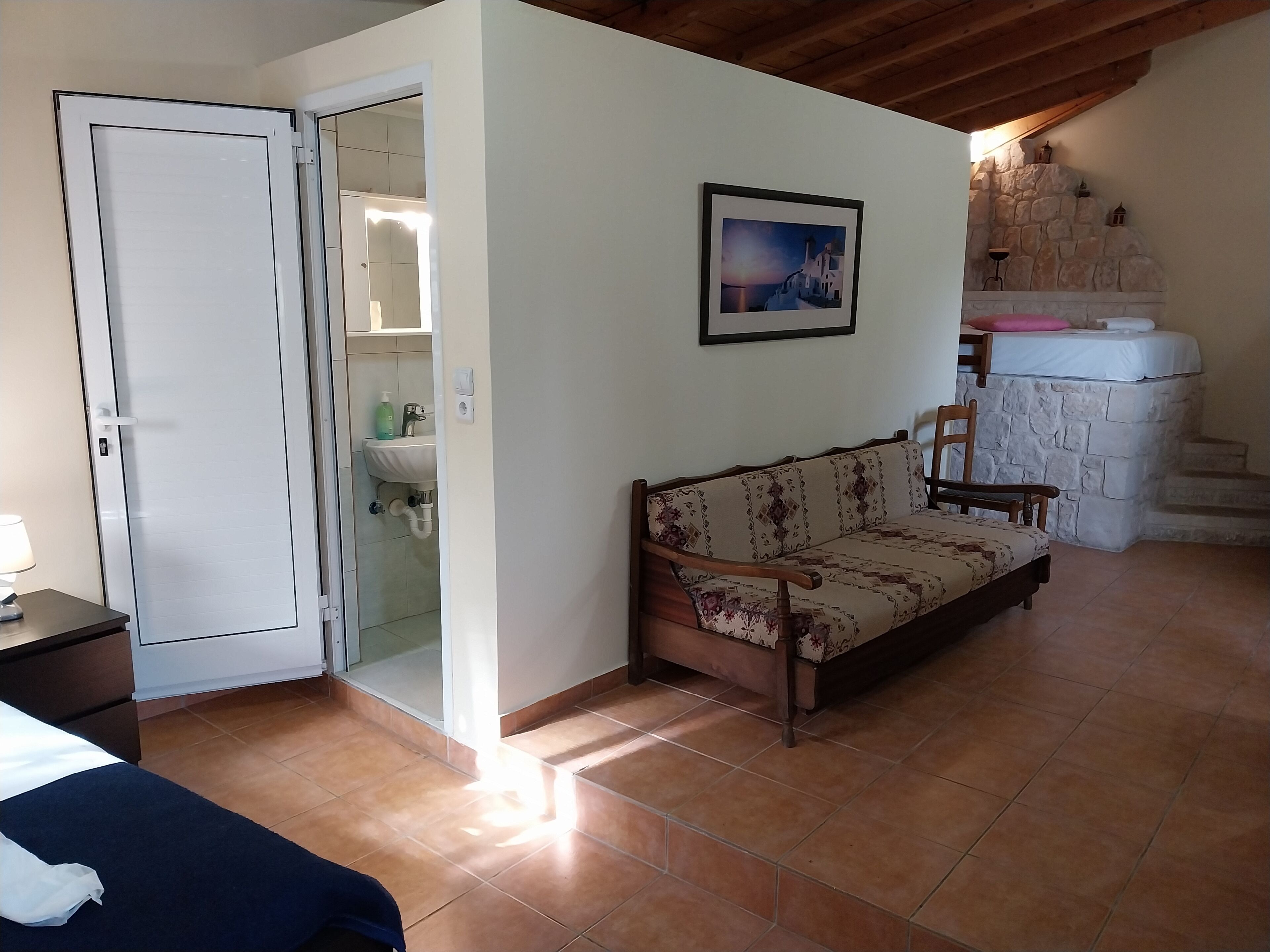 A room with a bed, a sofa, a bathroom with a sink, and a stone wall.