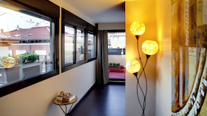 A corridor with large windows, a small table with items, and a wall with a textured mural. - THC Tirso Molina Hostel (Madrid)