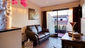 A living room with a brown leather sofa, a small table with a lamp, a vase with flowers, and a painting on the wall. - THC Tirso Molina Hostel (Madrid)