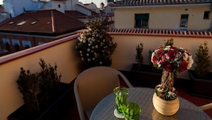 A balcony with a round table, two green glasses, a vase with red and white flowers, and potted plants. - THC Tirso Molina Hostel (Madrid)
