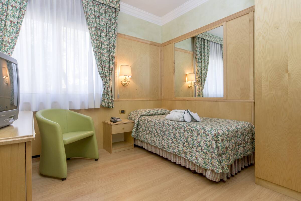 A hotel room with a bed, a desk, a chair, a TV, and a mirror.