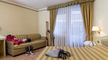 Una camera d'albergo con un letto, un divano, attrezzatura da sci e una finestra con tende.