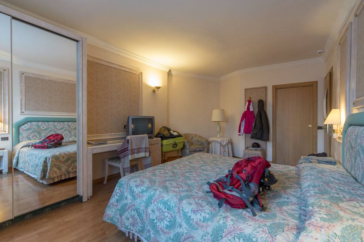 A hotel room with two beds, a desk, a television, a chair, a lamp, and a wardrobe.