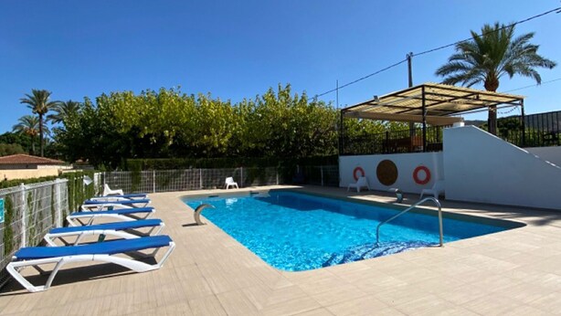 Une piscine avec des chaises longues, un espace de détente abrité et un ciel dégagé.