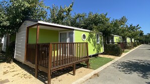 Une rangée de maisons mobiles, chacune dotée d’une terrasse en bois à l’avant, sous un ciel bleu azur, et entourées de pelouses verdoyantes.