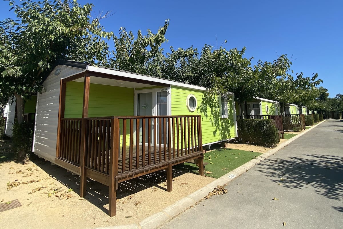 Filas de casas móviles con un porche de madera, cielo azul despejado y césped verde.