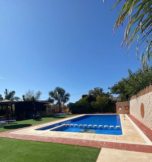 A rectangular swimming pool with a tiled deck, surrounded by a brick border and a grassy area. - Camping Armanello (Benidorm)
