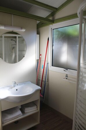 A bathroom with a white sink, mirror, and window. There are towels on a shelf and a broom leaning against the wall. - Camping Armanello (Benidorm)