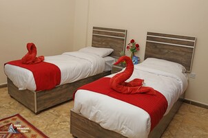 Two beds with wooden headboards, white bedding, and red towels shaped like swans.
