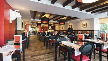Un restaurant doté d’un plancher en bois, de chaises noires et rouges, et de tables dressées pour le service.
