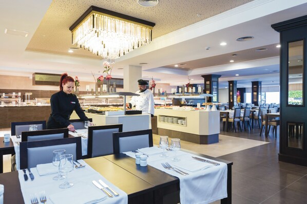 A modern dining area with a buffet, a chandelier, and a chef preparing food.