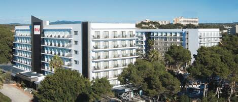 A modern hotel with multiple balconies, a swimming pool, and a view of the surrounding landscape.