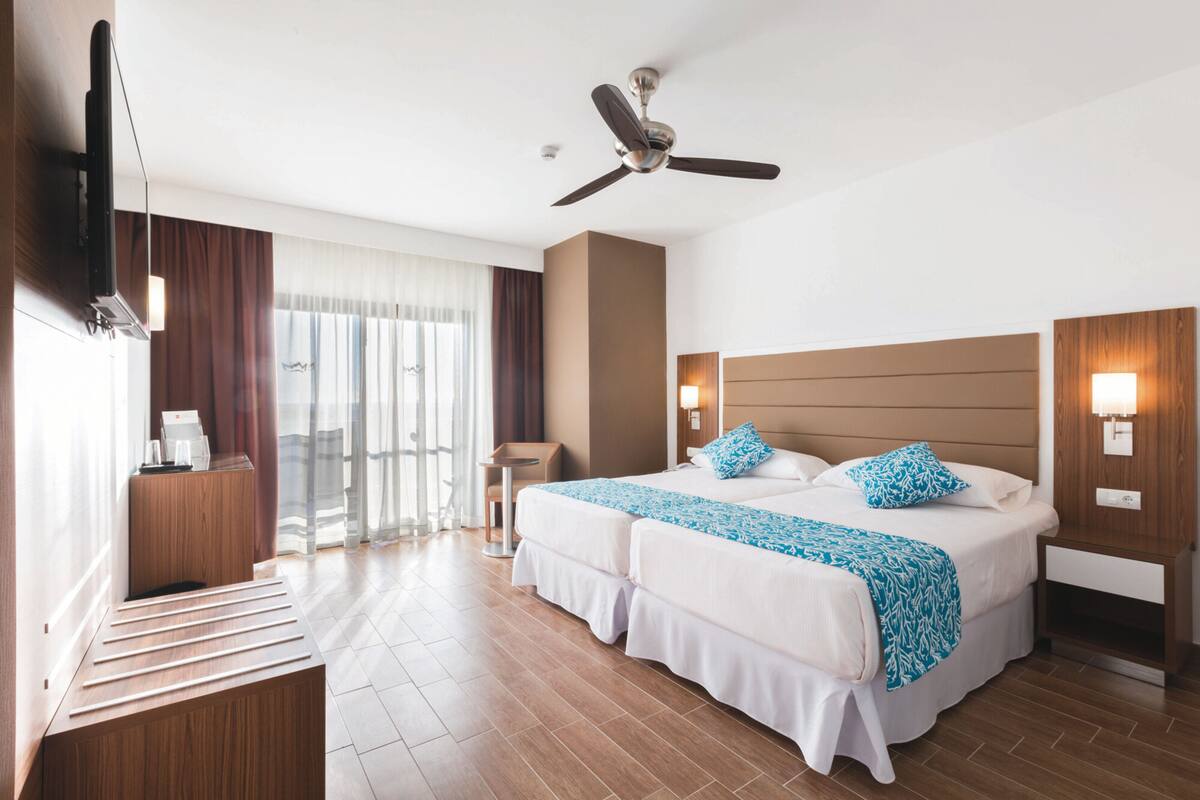 A hotel room with a large bed, a ceiling fan, a desk with a coffee machine, and a view of the outdoors.