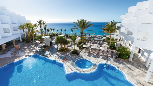 A resort pool area with multiple pools, palm trees, and a view of the ocean.