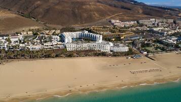 An aerial view of a coastal resort with a large hotel, sandy beaches, and clear turquoise waters.
