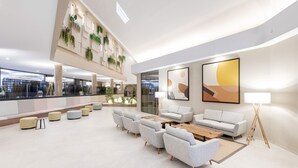 A spacious lobby with a high ceiling, modern seating, and a view of the cityscape through large windows.