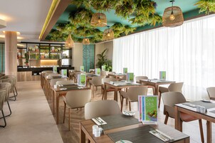 Un comedor moderno con mesas y sillas, una zona de bar con estanterías y un techo decorado con plantas colgantes.