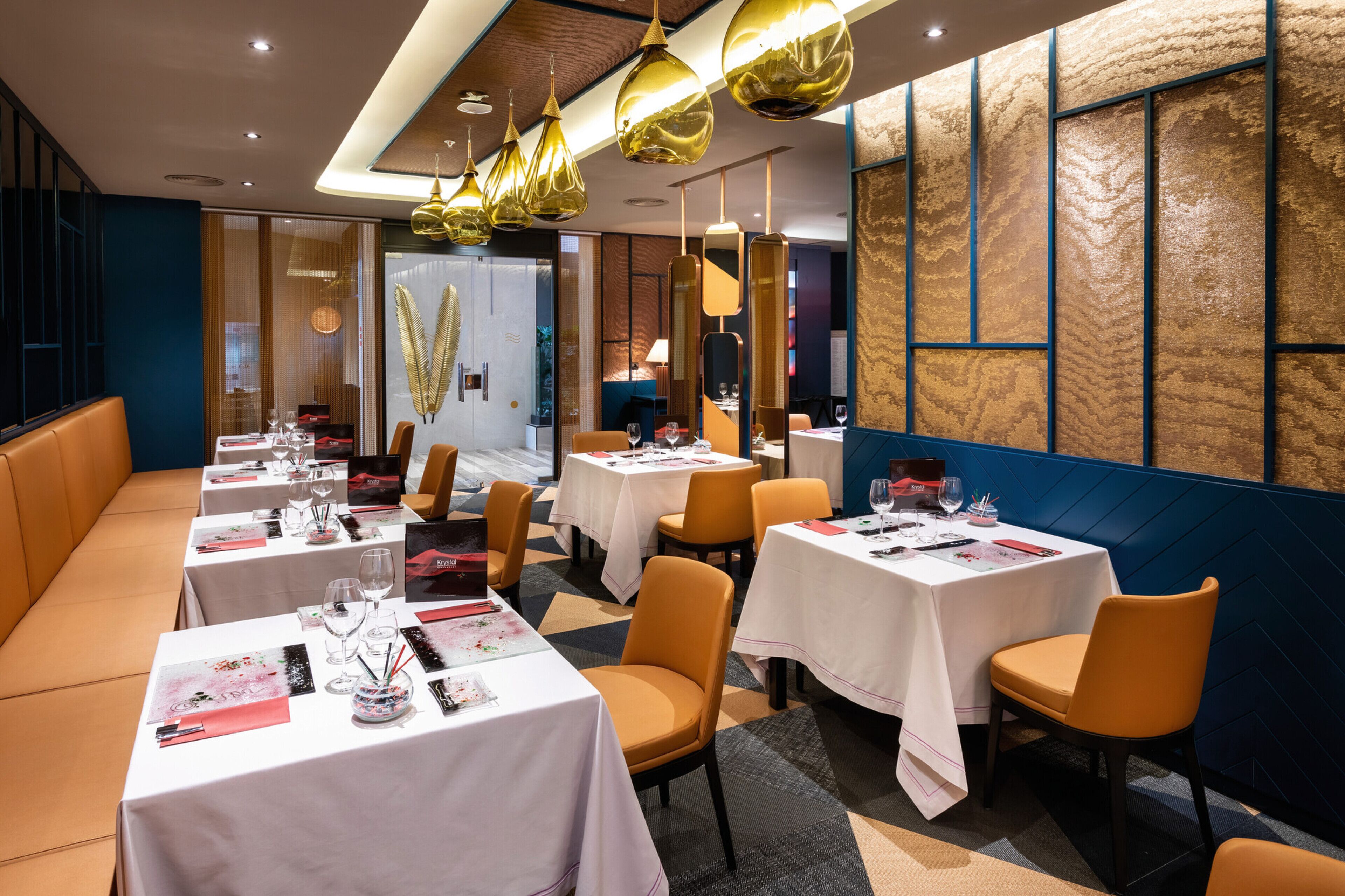 Un restaurante con varias mesas, sillas anaranjadas y lámparas colgantes doradas.