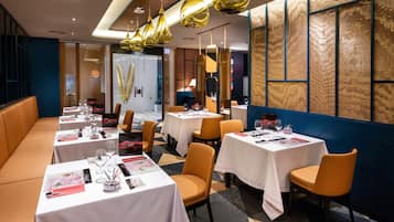 Un restaurante con varias mesas, sillas anaranjadas y lámparas colgantes doradas.