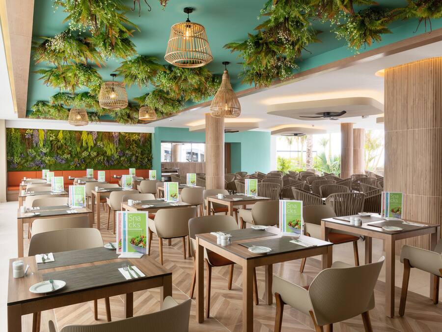 A restaurant with tables and chairs, a green wall with plants, and hanging lights.