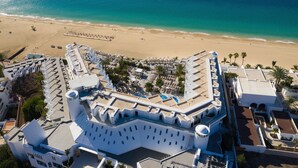 A coastal hotel with a white facade, multiple balconies, and a beach view.