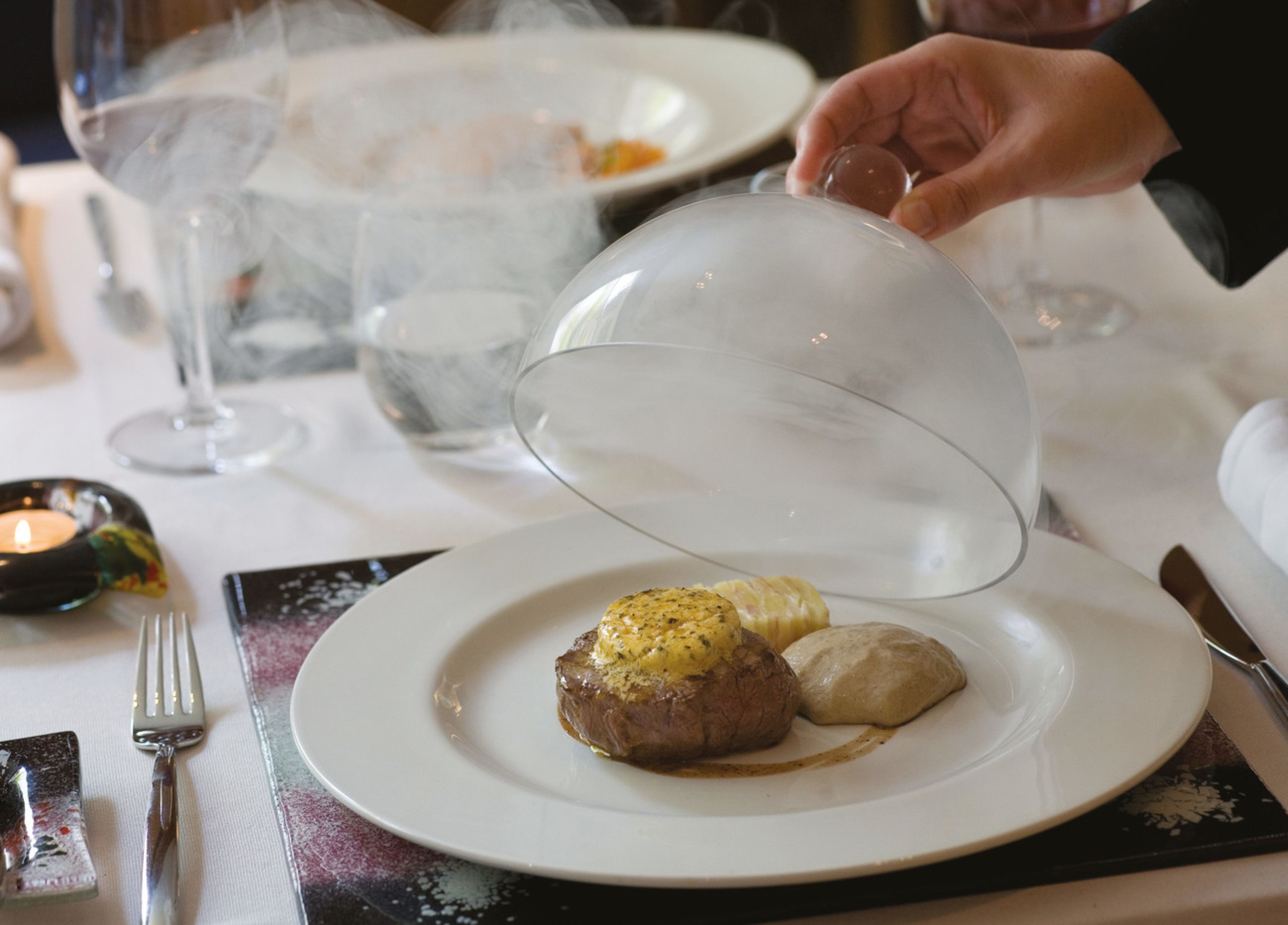 A dining table with a plate of food, a glass of water, and a candle.
