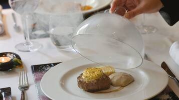 A dining table with a plate of food, a glass of water, and a candle.
