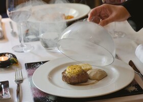 A dining table with a plate of food, a glass of water, and a candle.