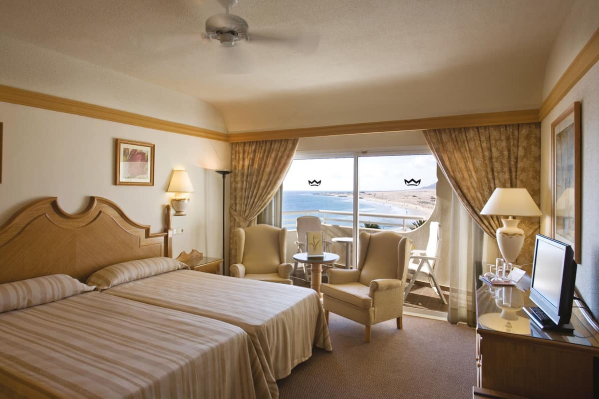 A hotel room with a large bed, two armchairs, a small table, and a TV.