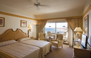 A hotel room with a large bed, two armchairs, a small table, and a TV.