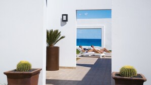 A doorway leading to a pool area with two people relaxing on sun loungers, surrounded by potted cacti. - Hotel Riu Palace Tres Islas (La Oliva)