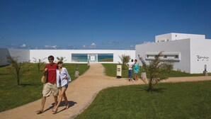 A pathway leading to a modern building with a view of the ocean. - Hotel Riu Palace Tres Islas (La Oliva)