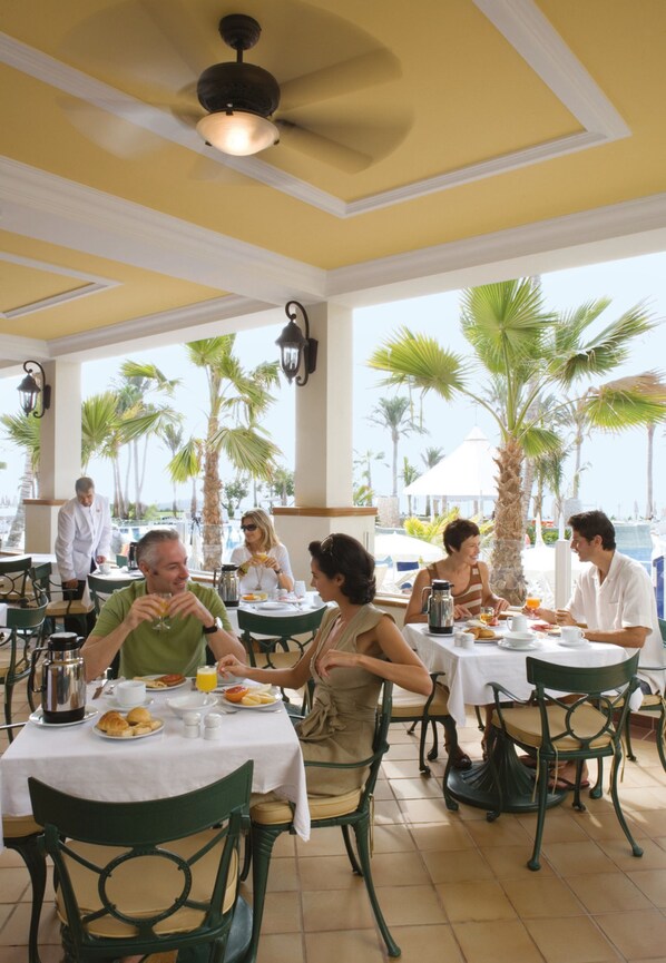 A restaurant with outdoor seating, palm trees, and a view of the sea.