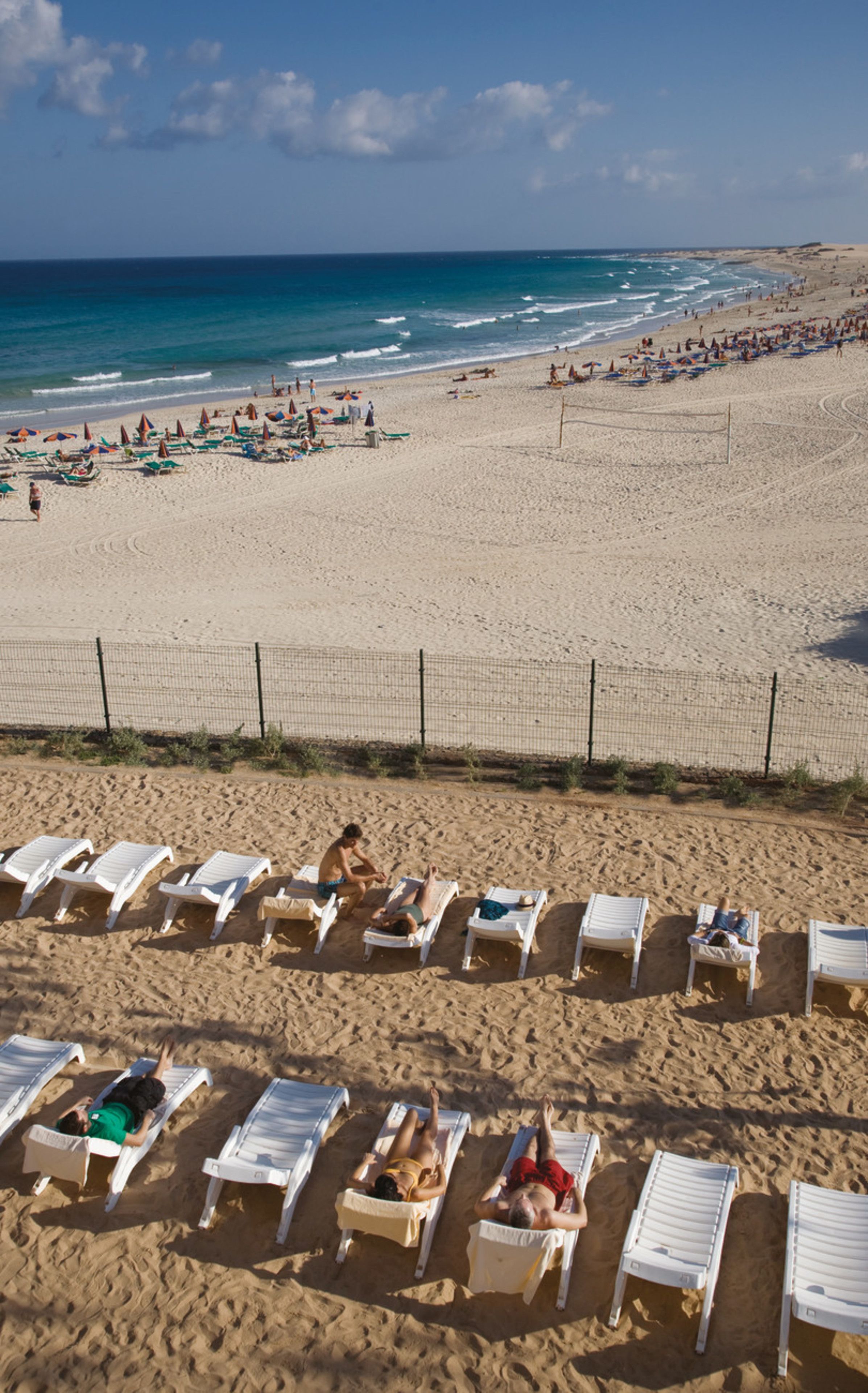 Ein Strand mit Liegestühlen und Sonnenschirmen, ein sandiger Uferstreifen und das Meer im Hintergrund.