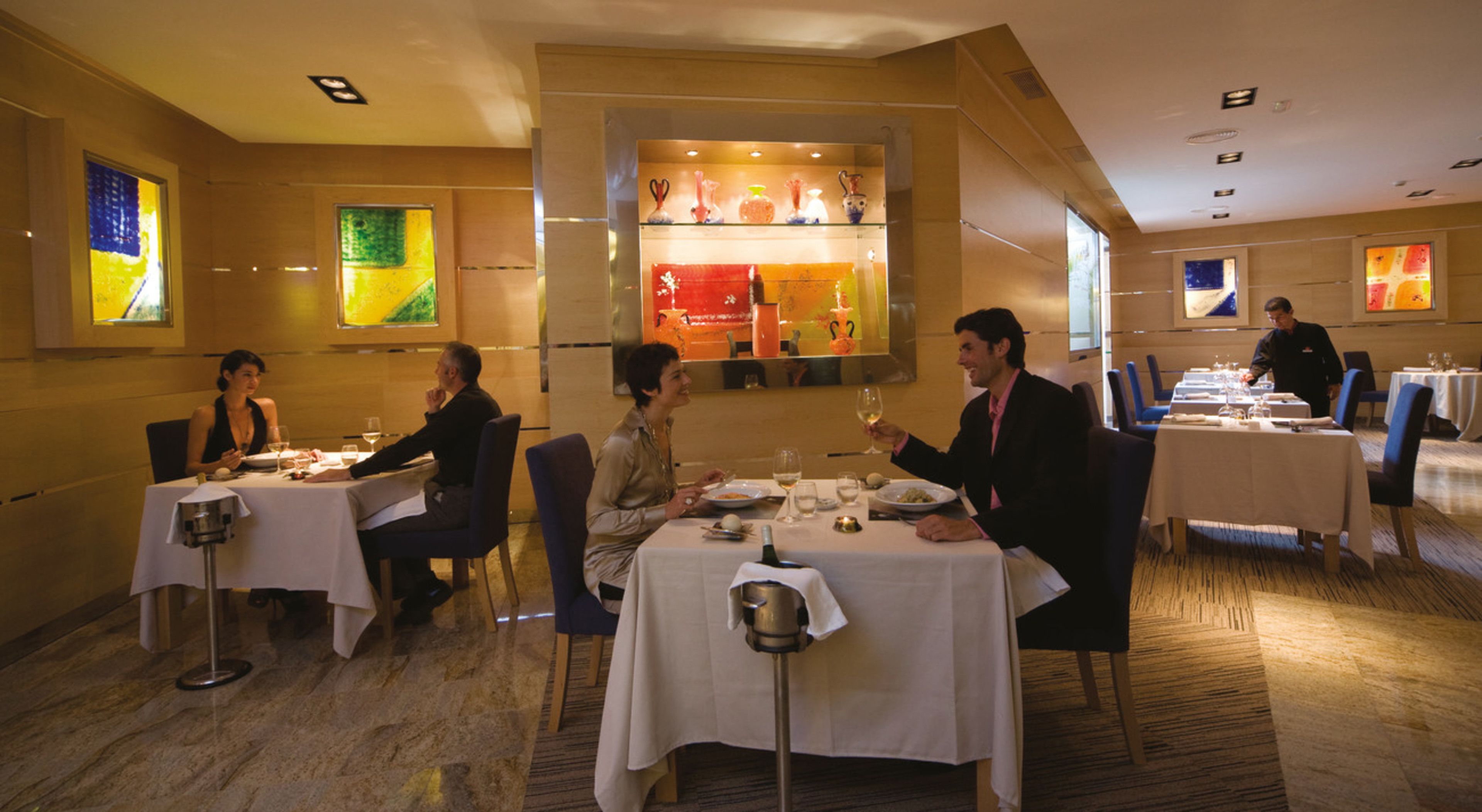 Un restaurante con varias mesas, cada una con manteles blancos y cubertería.
