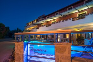 A hotel exterior with a swimming pool, outdoor seating, and a sign reading "Dante's Maisonettes".