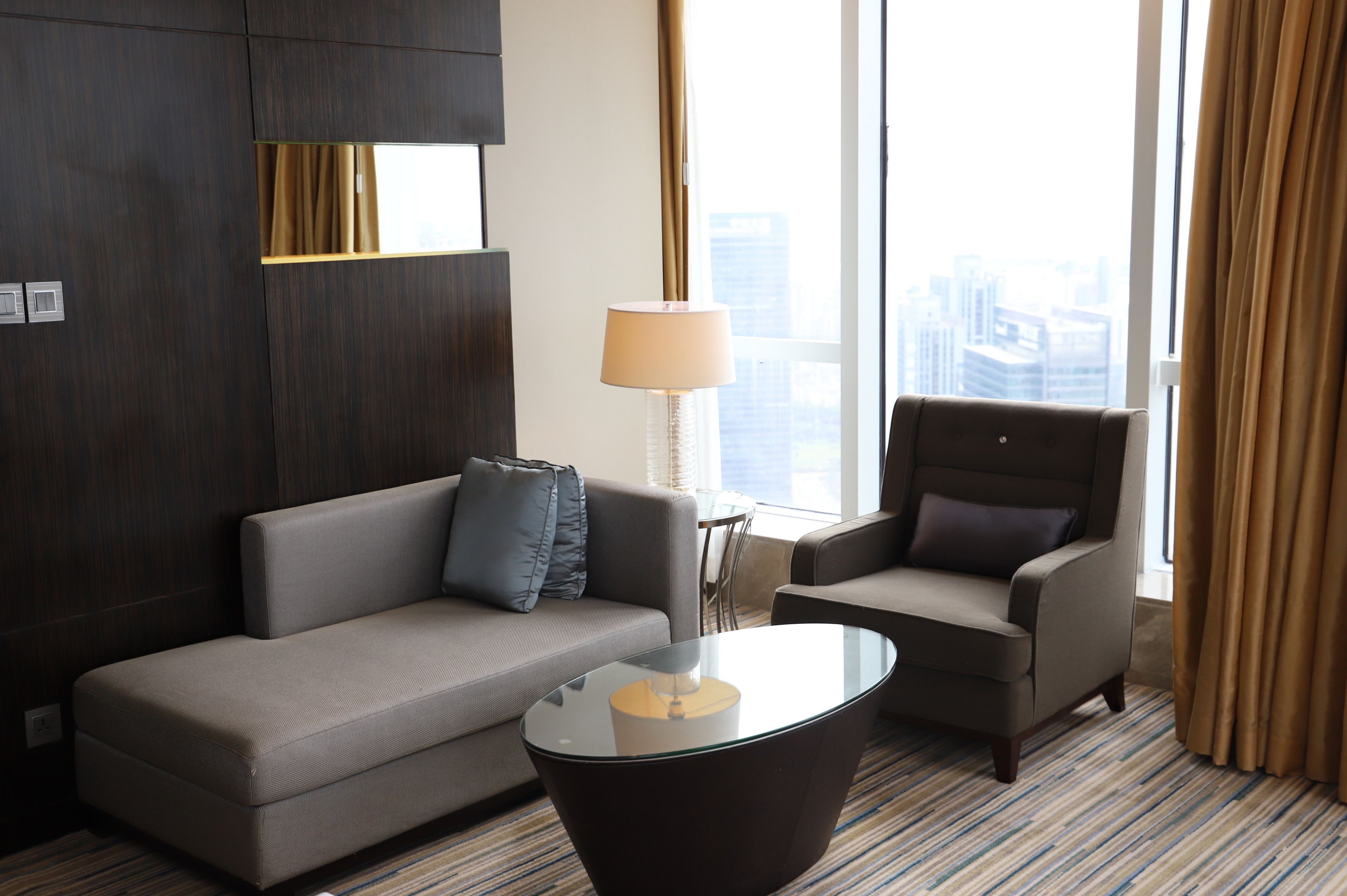 A modern hotel room with a sofa, armchair, and a glass coffee table.