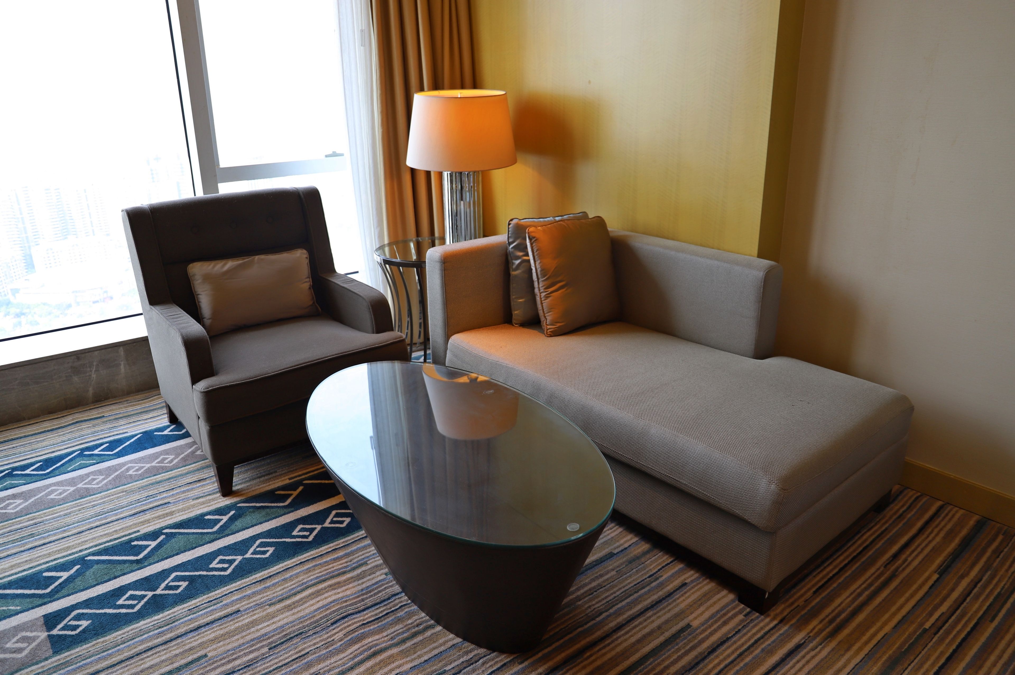 A hotel room with a sofa, armchair, and a glass coffee table.
