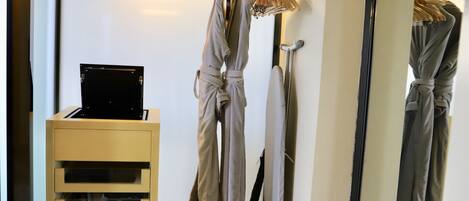 A hotel room with a bed, a bedside table with a laptop, and a wardrobe with hanging clothes.