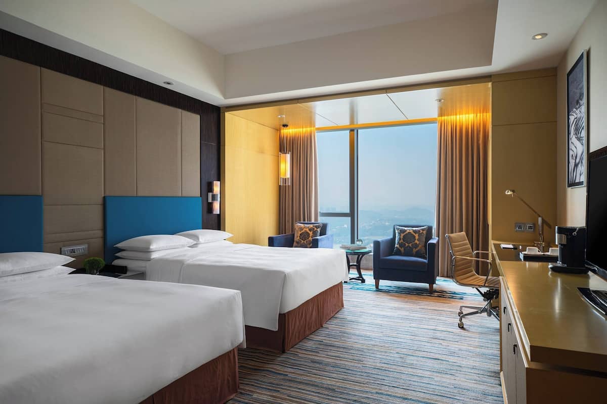 A hotel room with two beds, a desk, a chair, a small table, and a large window with curtains.