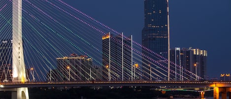 A cable-stayed bridge with illuminated cables, a river below, and modern buildings in the background.