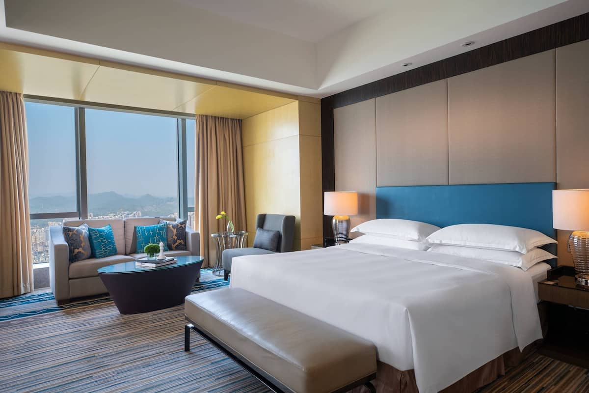 A hotel room with a large bed, a sofa, a coffee table, and a view of the city.
