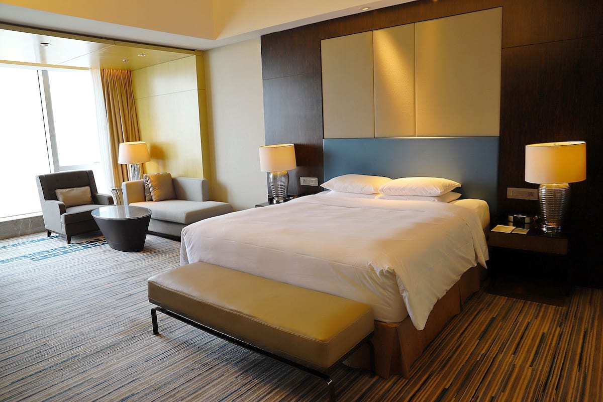 A hotel room with a large bed, a sofa, a bench, two lamps, and a large mirror.