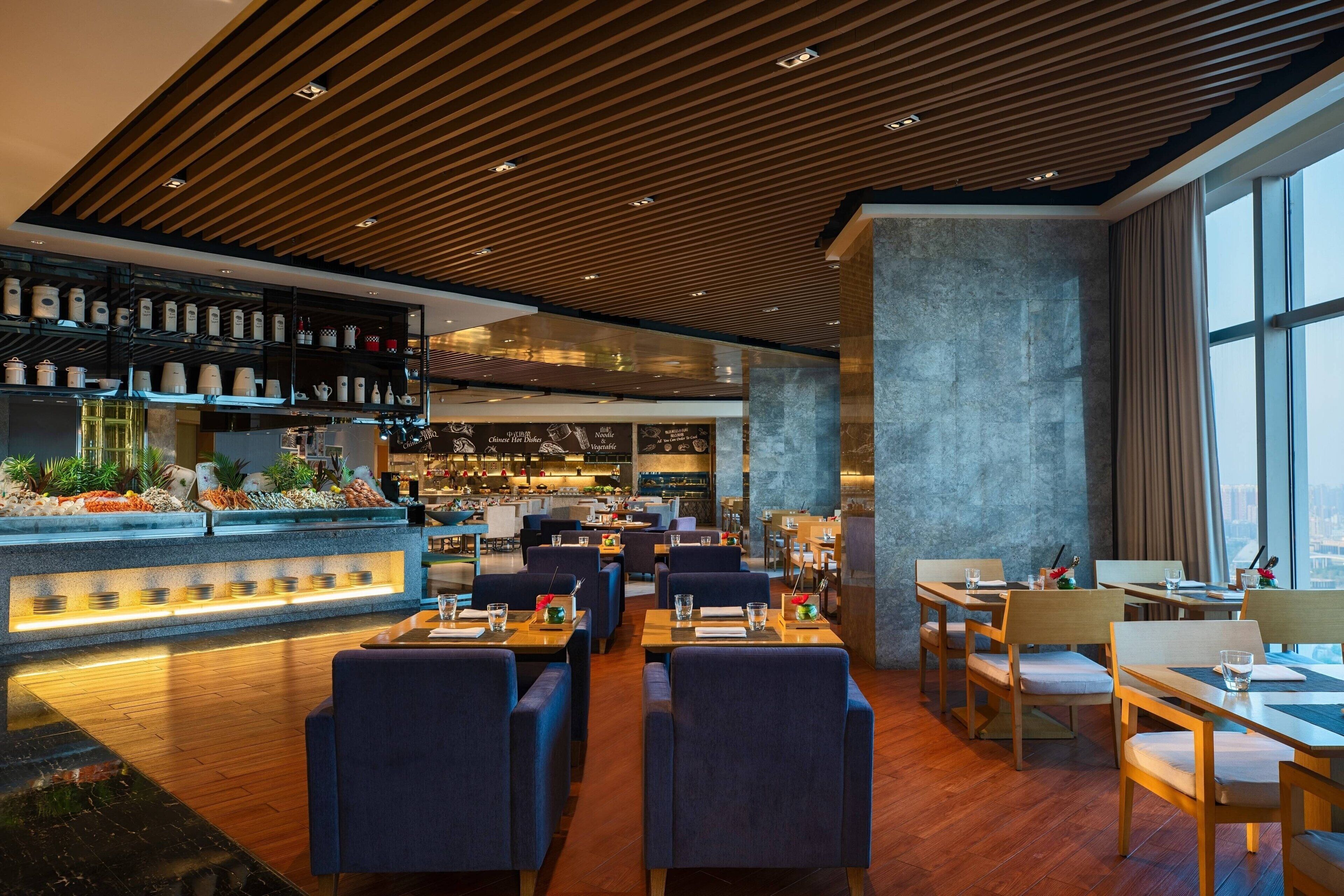 A modern restaurant with wooden ceiling panels, a bar area with shelves of bottles, and seating arrangements.