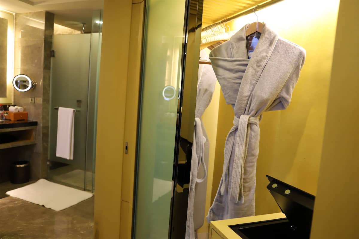 A bathroom with a glass shower enclosure, a white towel on the floor, and a robe hanging on a rack.