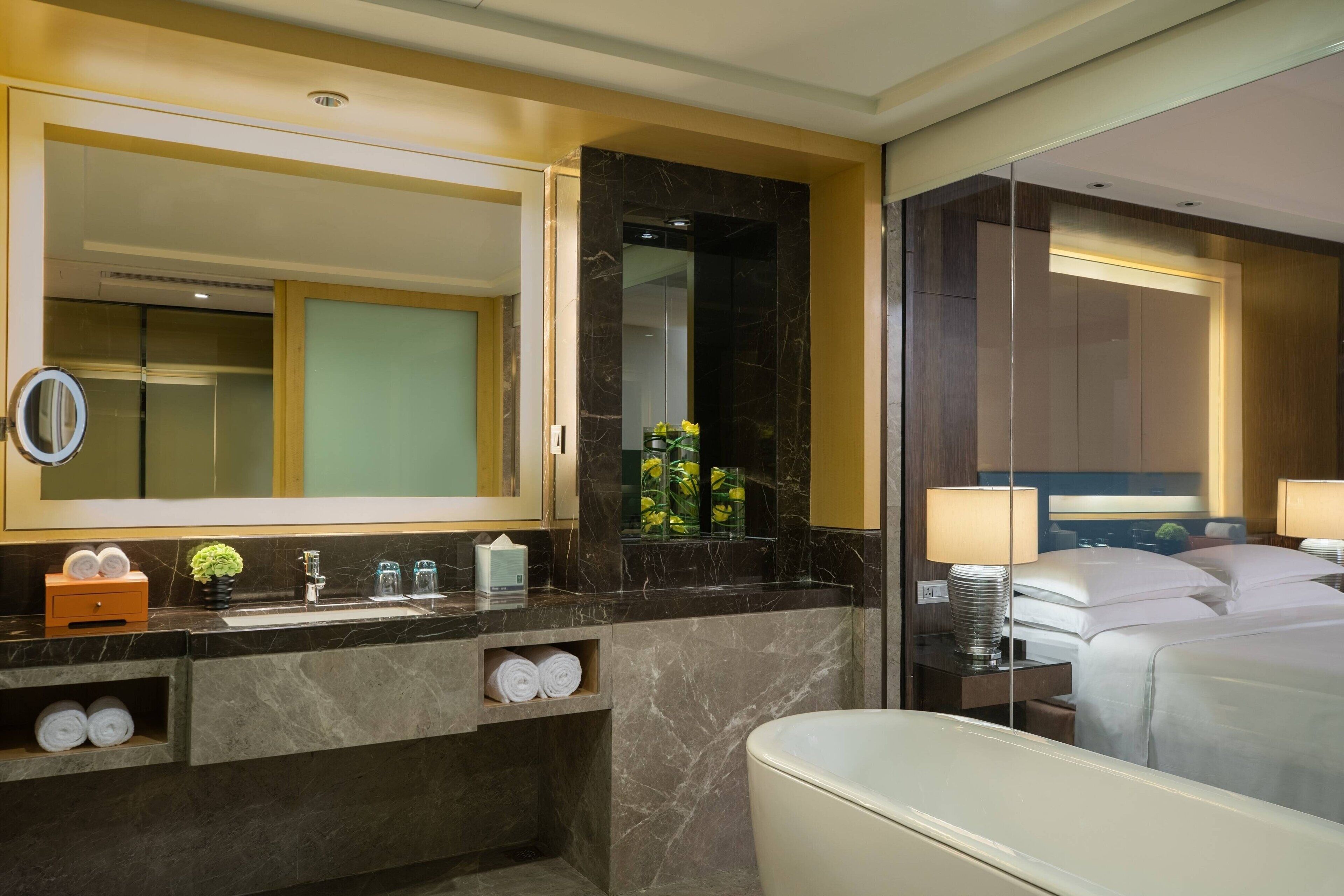 A modern hotel bathroom with a large mirror, marble countertop, and a bathtub.