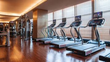 Un gimnasio con cintas de correr, máquinas de ejercicio y ventanas amplias con persianas.